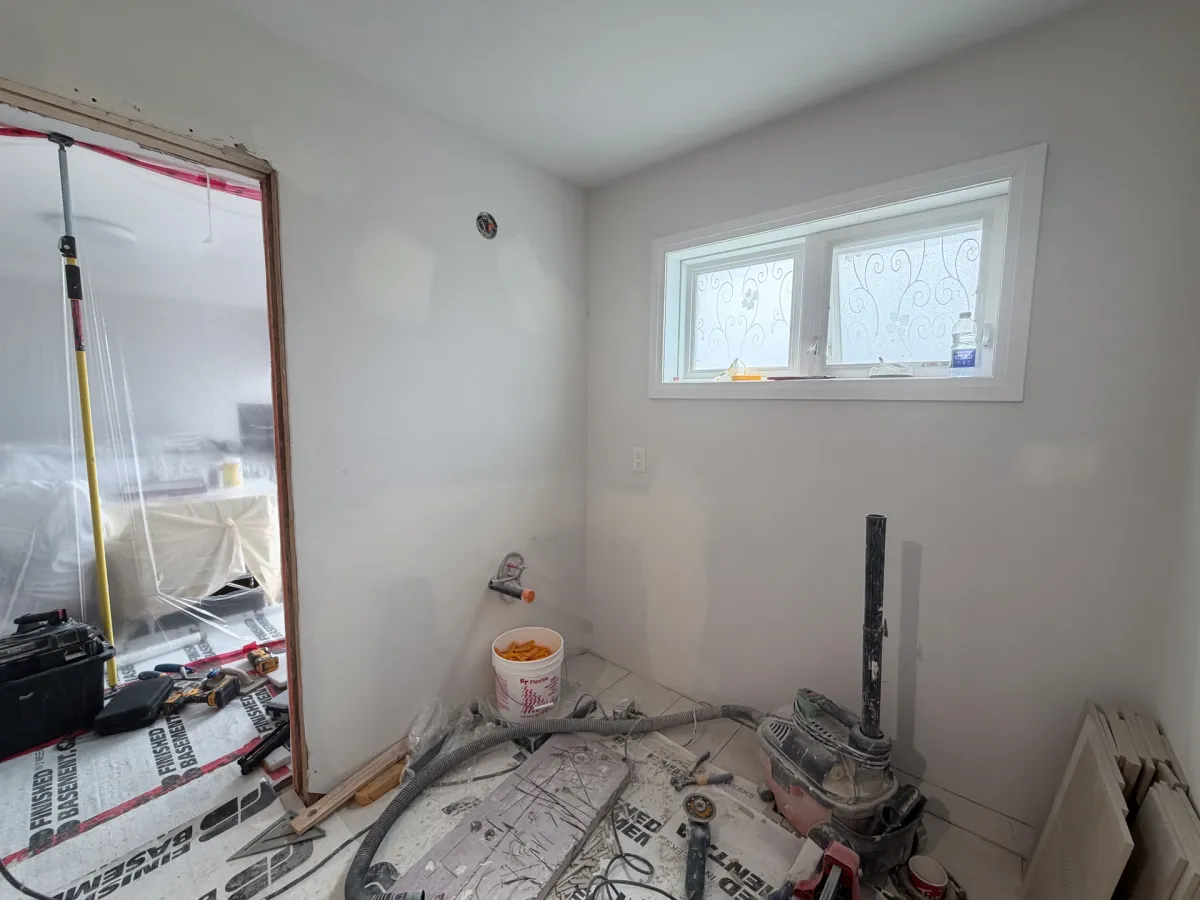 The bathroom gutted to bare walls, floor protected, plumbing roughed in