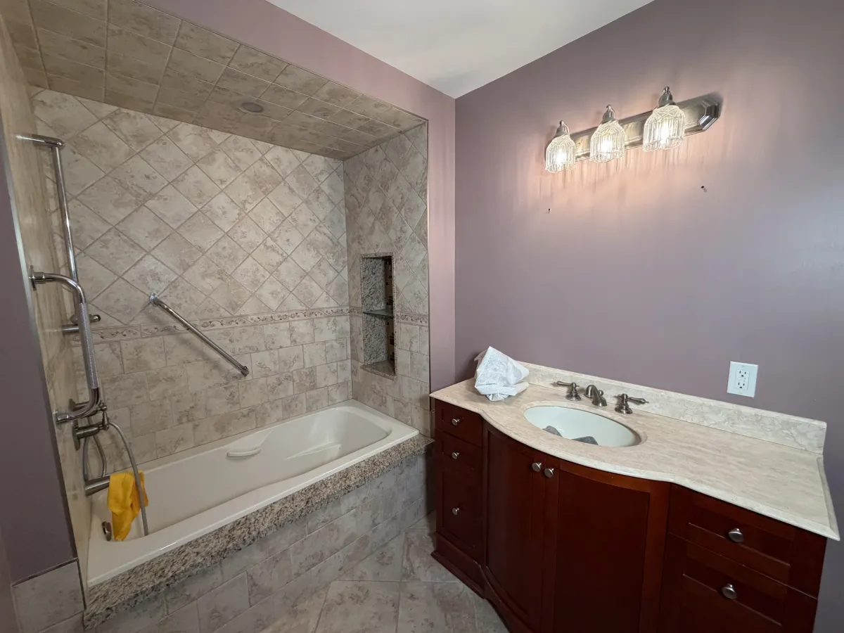 Before: the old alcove tub with a grab bar on the tile, a cherry vanity with a cultured-marble top and mauve walls