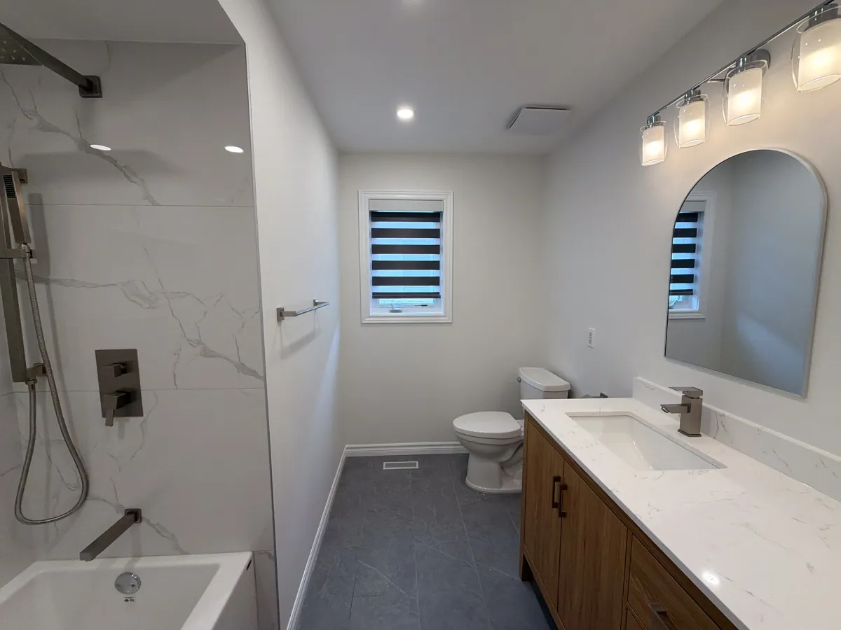 After: the marble-look tub and shower with a rain head, an oak vanity under an arched mirror and the new toilet on grey tile