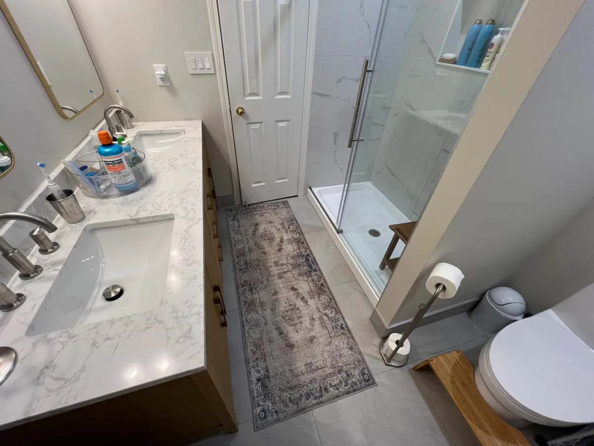 After: an oak vanity with a marble-look top and brushed-gold taps, a gold-framed mirror and the glass walk-in shower