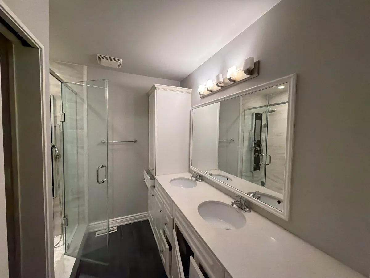 Before: the builder-grade room, with a white laminate vanity, a wide plain mirror and a framed glass stall