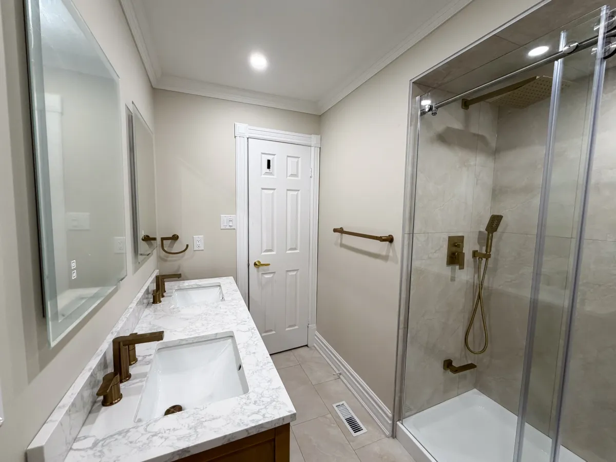 After: an oak double vanity with a marble-look quartz top and brushed-gold taps, beside the sliding glass shower with gold fittings