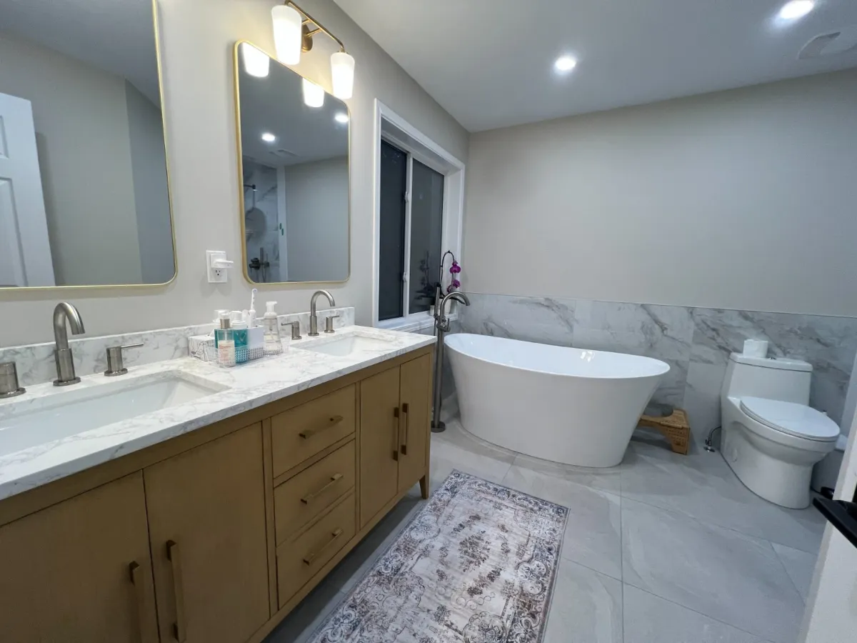 After: an oak double vanity with a marble-look top, the new freestanding tub, the toilet and the marble-look shower beyond