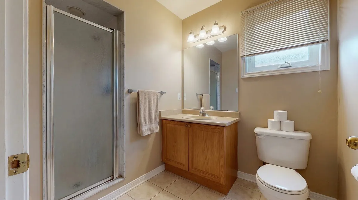 Before: a beige bathroom with an oak vanity, a framed shower stall with a frosted door and a plain mirror over the sink