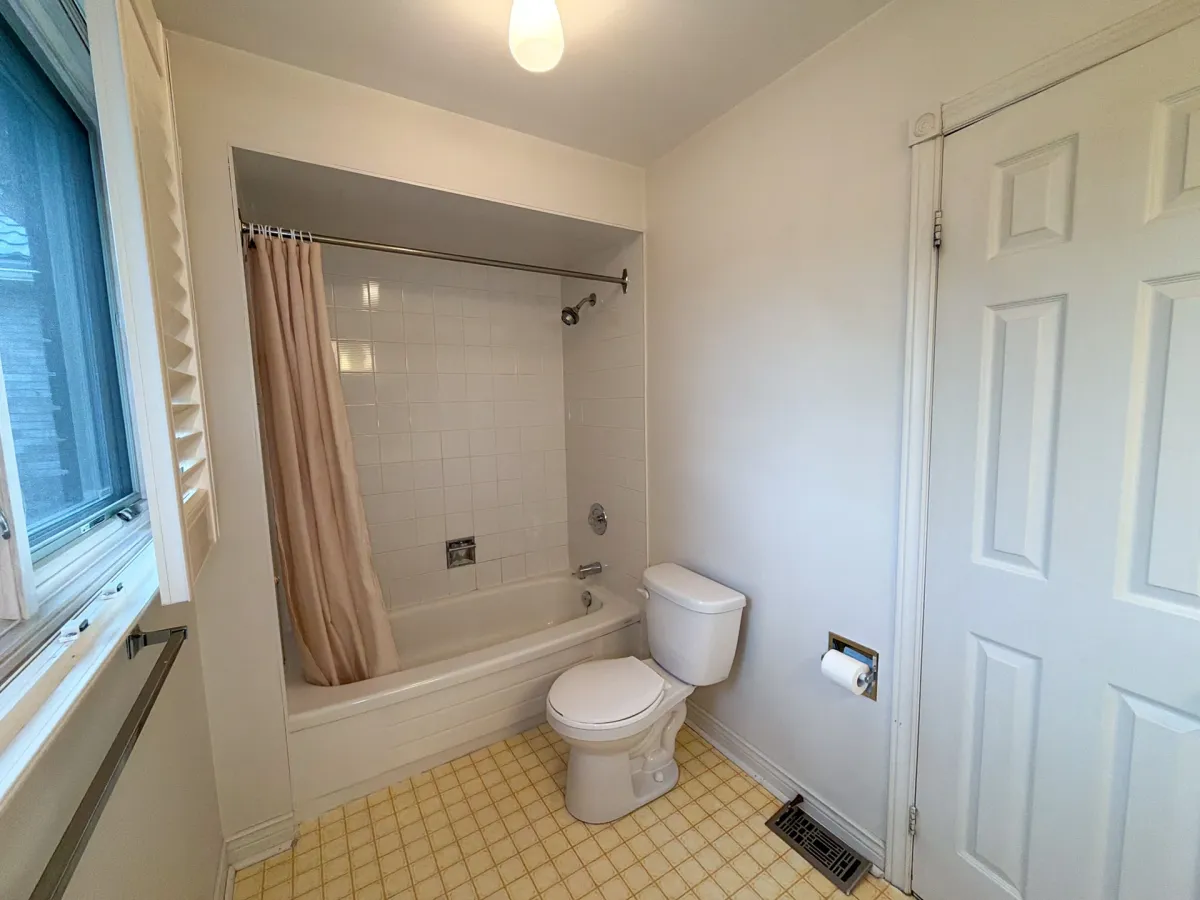 Before: a peach shower curtain over the alcove tub, yellow floor tile, the old toilet and a beige door
