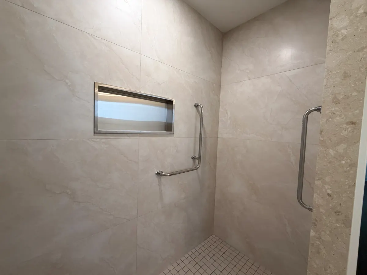 Barrier-free shower tiled in large-format stone-look porcelain, with two stainless grab bars and a level mosaic floor