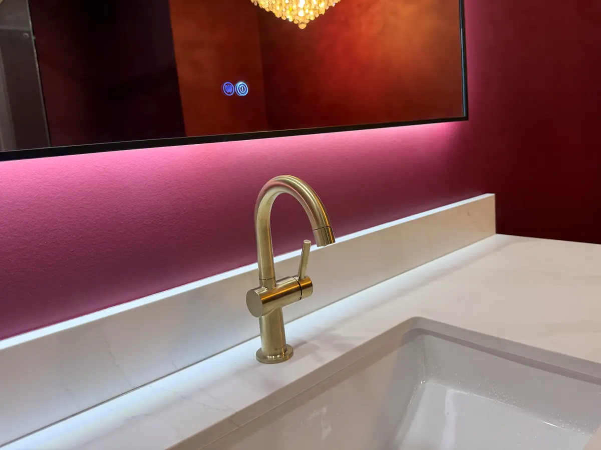 Close-up of a brushed brass tap on a quartz vanity top, under a backlit mirror on a deep red wall