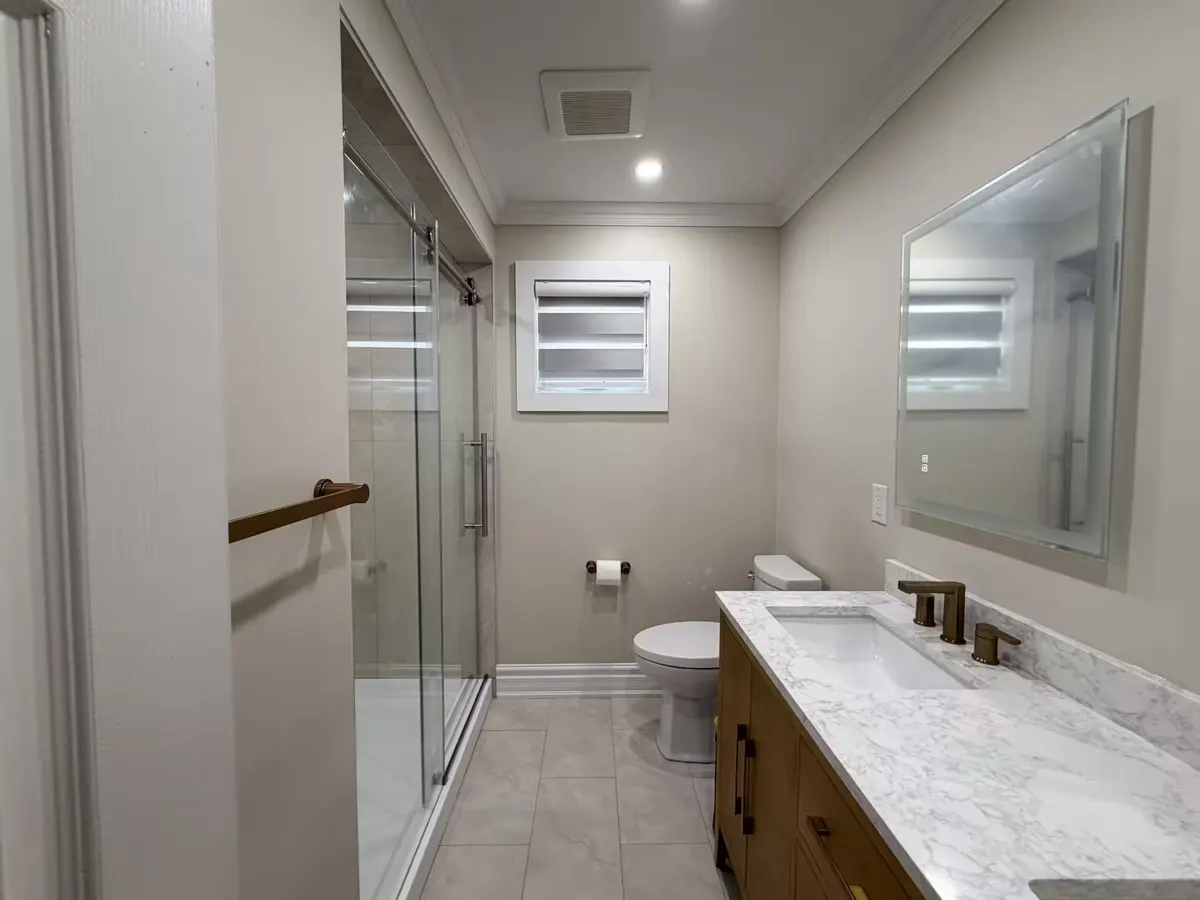 Marble-look sliding-glass shower beside a white oak vanity with a marble counter and brushed-brass taps