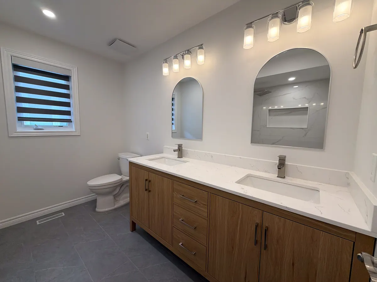 Family bathroom with a walnut double vanity, quartz counters, arched mirrors and sconce lighting, the tiled shower reflected in the mirror