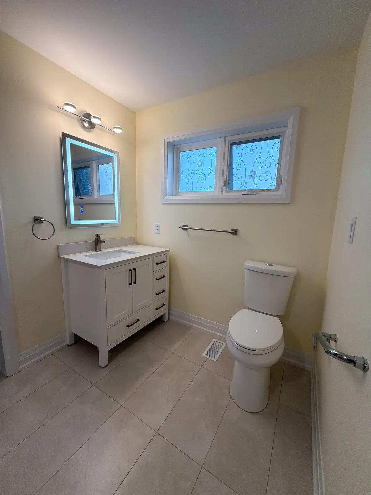 Bathroom with a white shaker vanity under a backlit mirror, a comfort-height toilet and frosted privacy windows