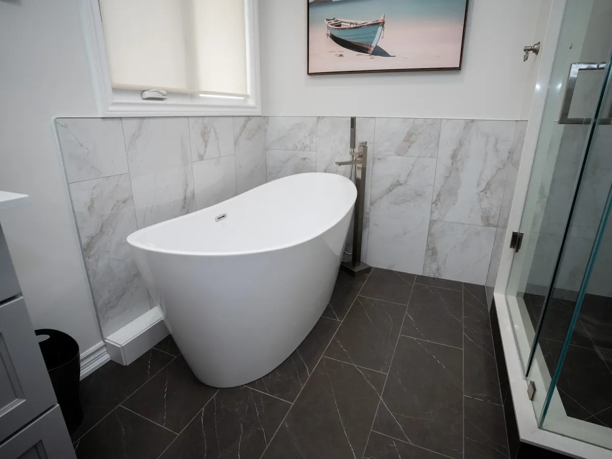 Freestanding tub against marble-look wall tile beside a glass corner shower, on a dark slate-look floor