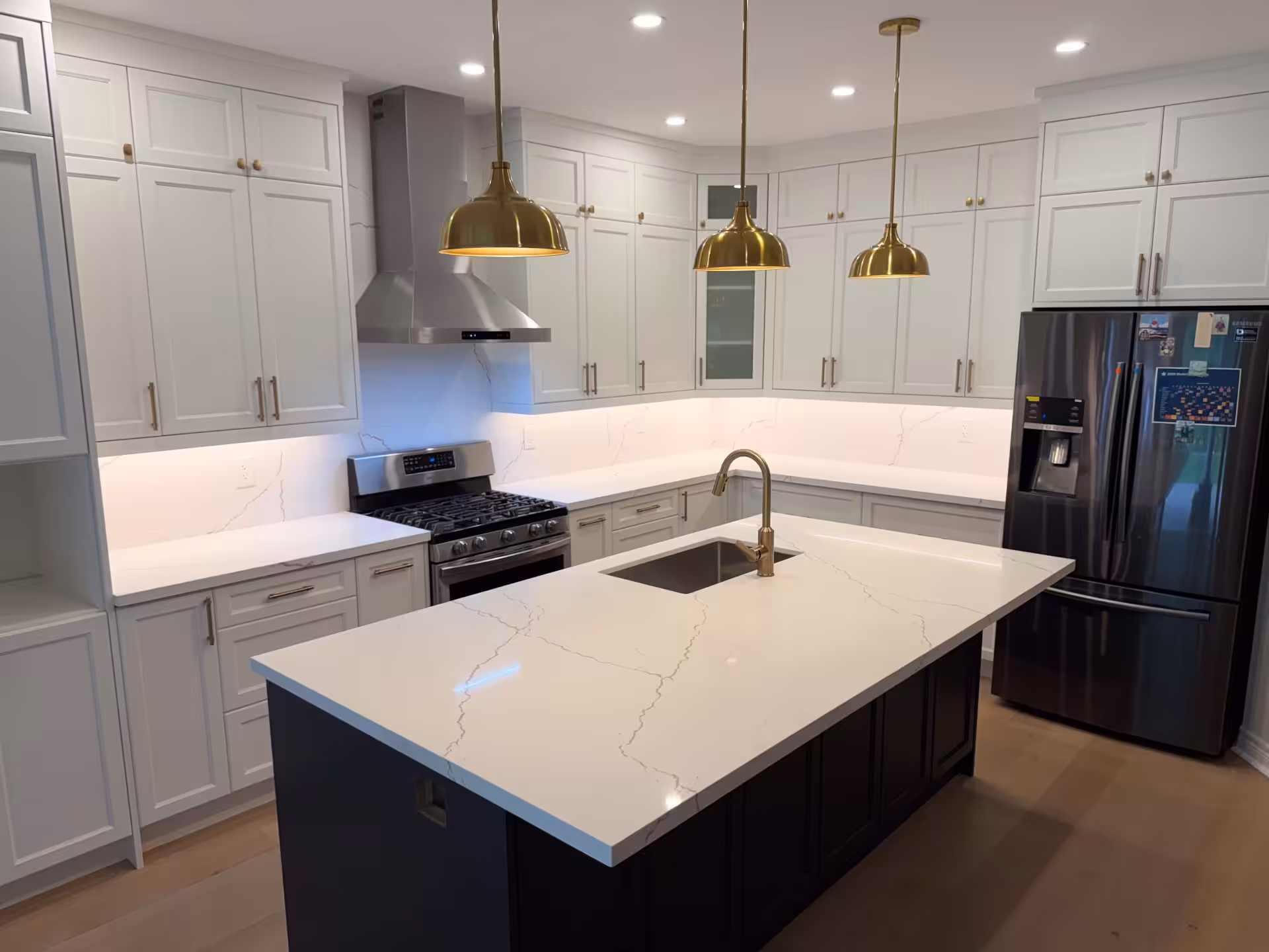 Kitchen with dark island, marble counters and brass pendant lights
