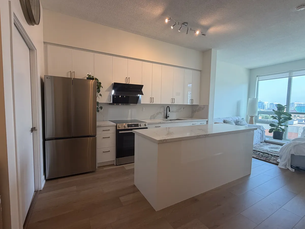 After: high-gloss white cabinets, a quartz counter and backsplash, a black hood and a new quartz-topped island, with the city beyond the window