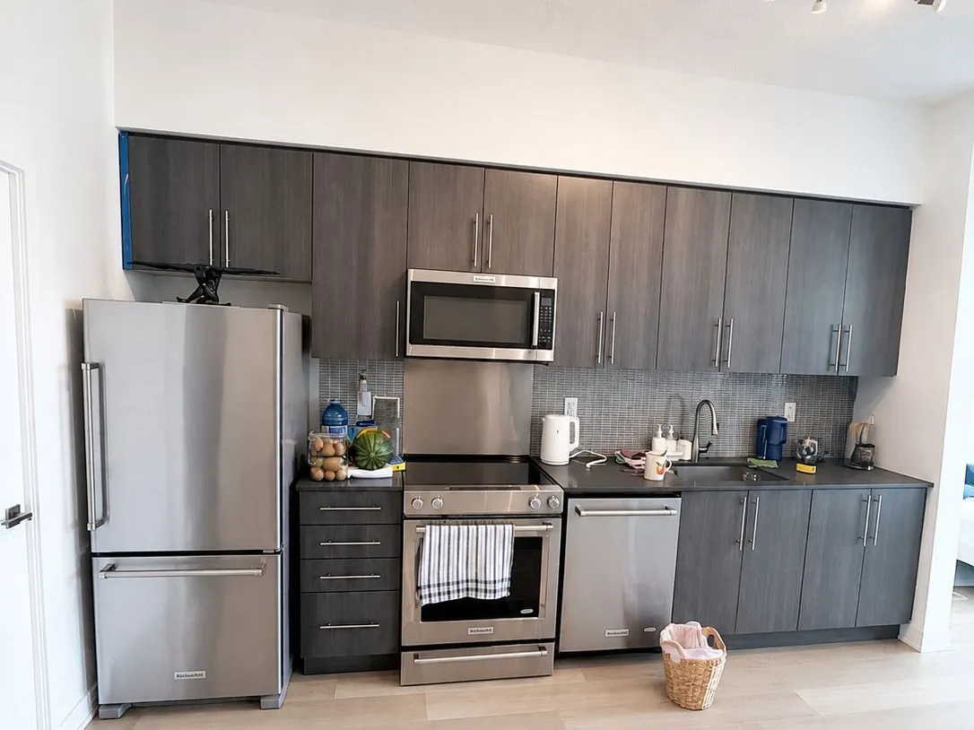 Before: a builder condo kitchen - one wall of grey slab cabinets, a dark counter and a grey mosaic backsplash