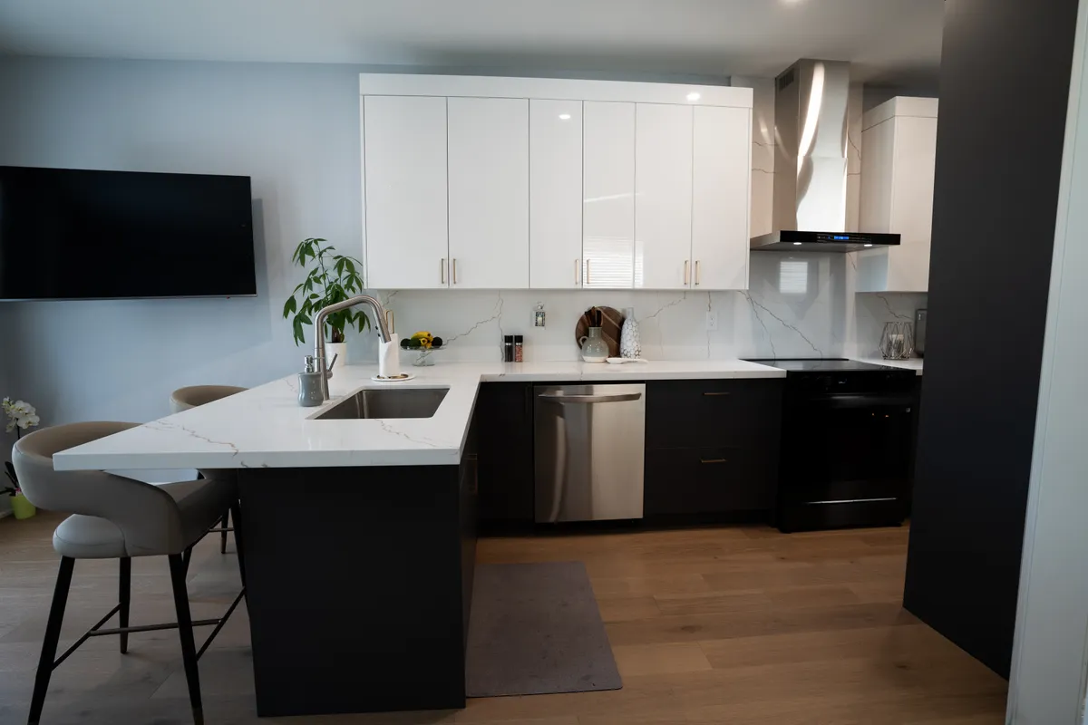 After: gloss white uppers over charcoal bases, a quartz peninsula with two stools and a stainless hood, on new wide-plank flooring