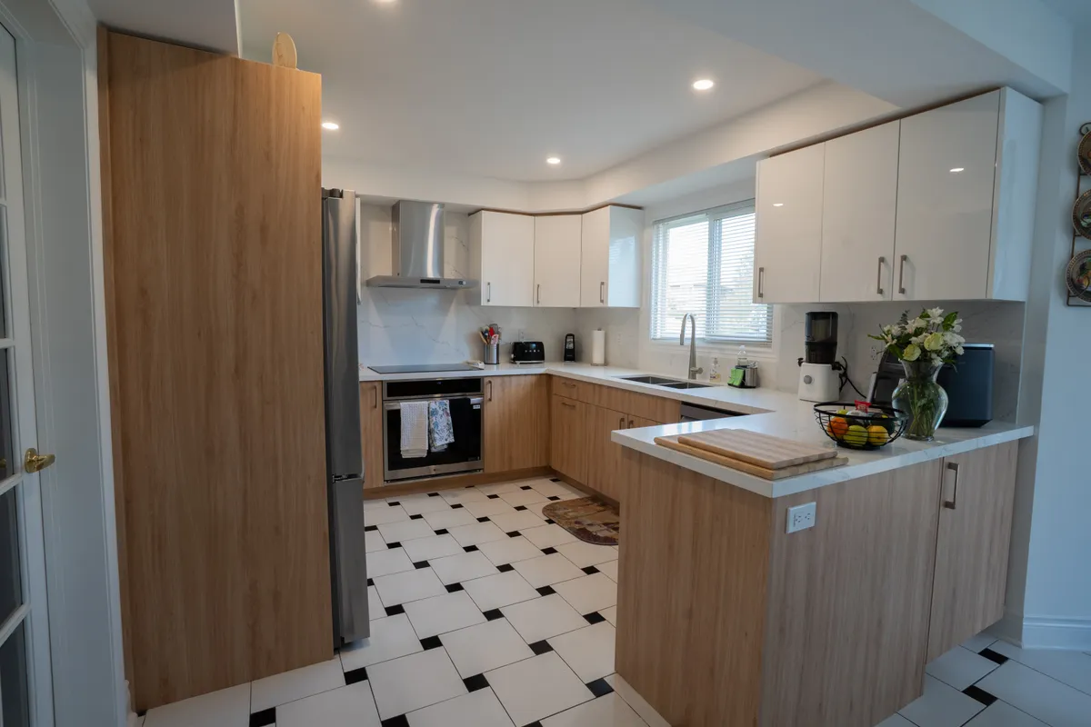 After: high-gloss white uppers and oak-grain bases in the same U, with a quartz peninsula and a stainless hood, on the original tile floor