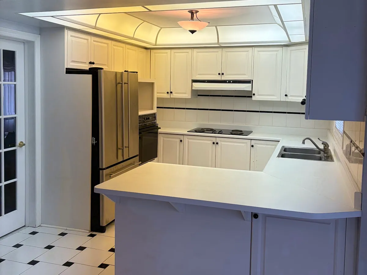 Before: white raised-panel cabinets under a dropped light box, a laminate peninsula and the black-and-white tile floor
