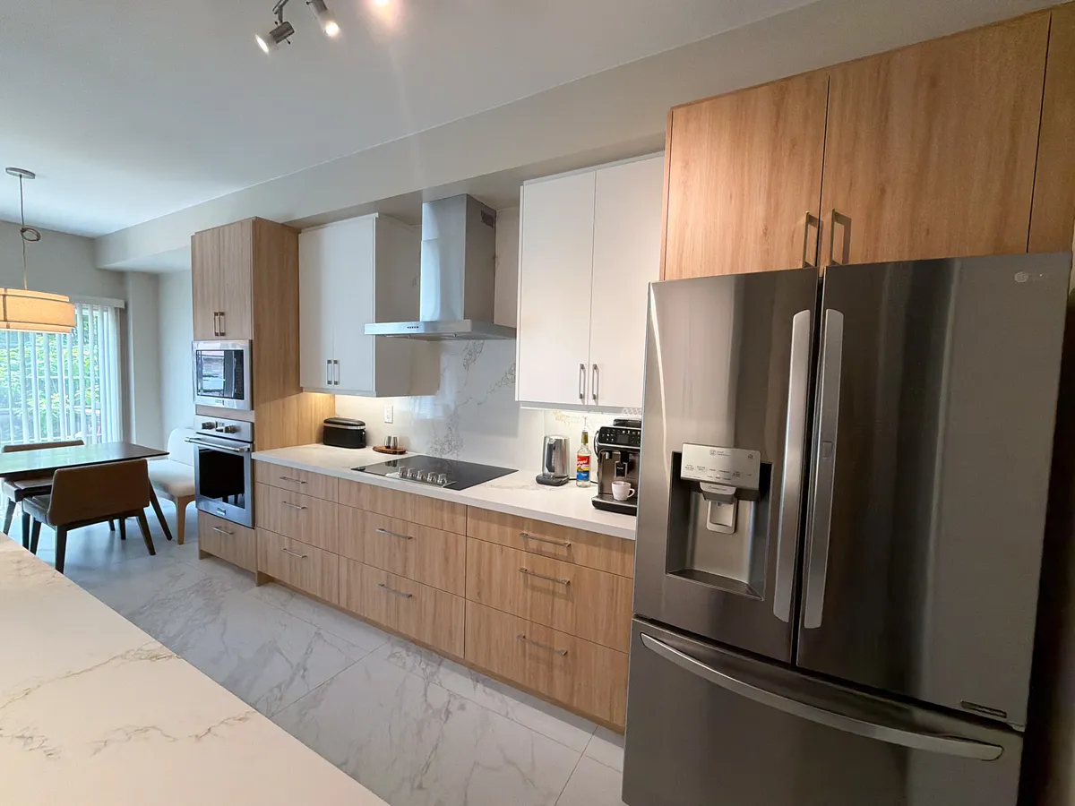After: oak-grain base cabinets under pale grey uppers, a stainless hood over the cooktop and the fridge, seen from the dining end
