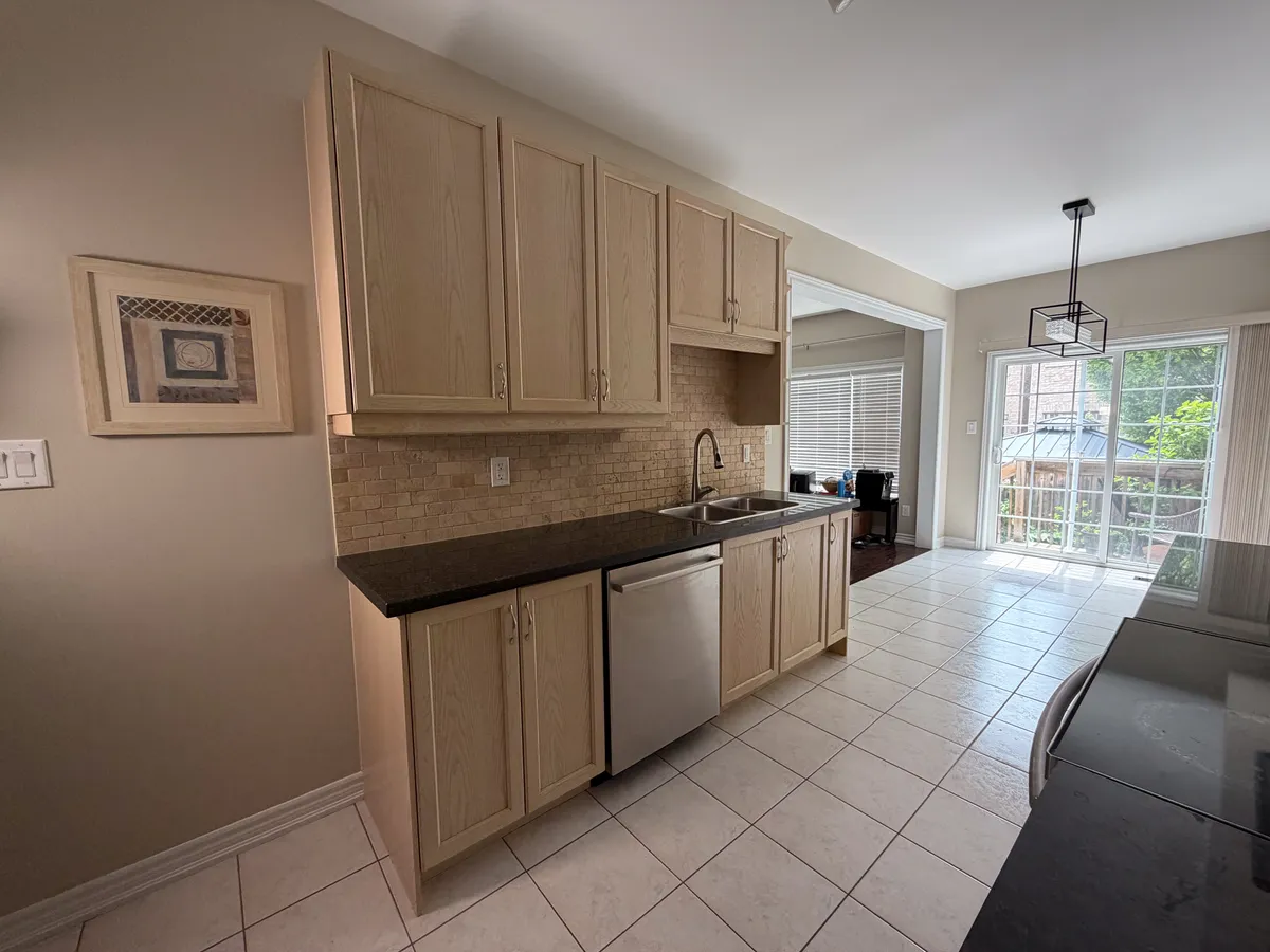 Before: a galley kitchen with maple cabinets, black granite counters and beige ceramic tile, looking towards the patio door