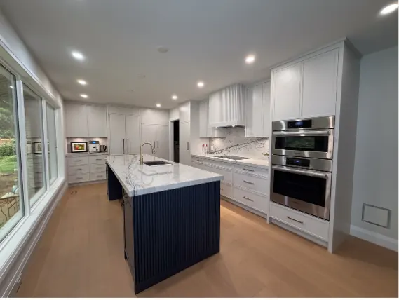 White kitchen with a navy island, marble waterfall counter and a wall of windows