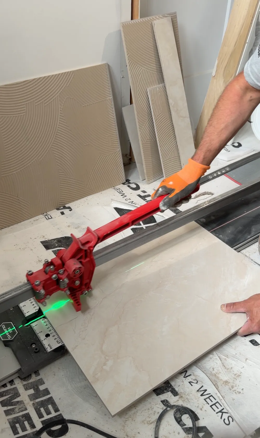A large-format porcelain tile being scored on the rail cutter, the floor protected