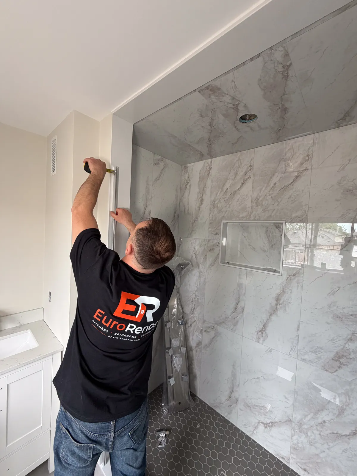One of our tilers setting the last marble-look wall tiles in a shower with a recessed niche, the hex mosaic floor already down