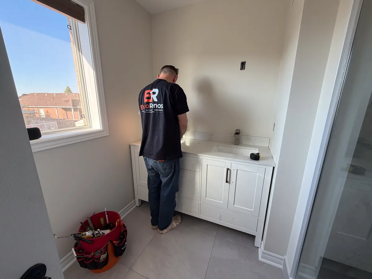 One of our crew fitting a white vanity under the window of a finished bathroom, the tile already down