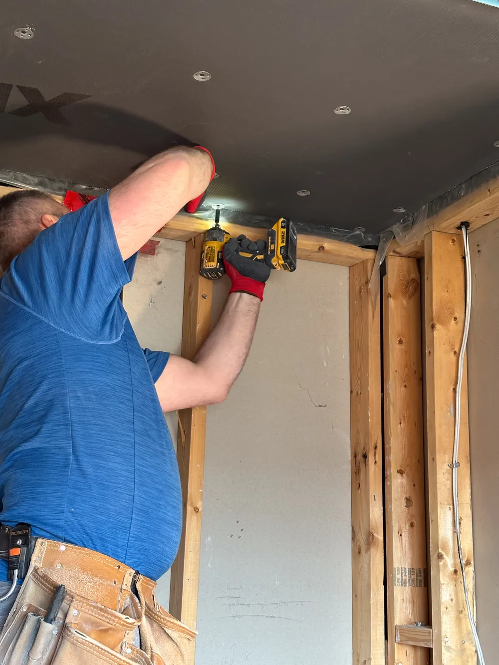 A crew member screwing waterproof XPS-TEK backer board to the shower walls, the ceiling already boarded