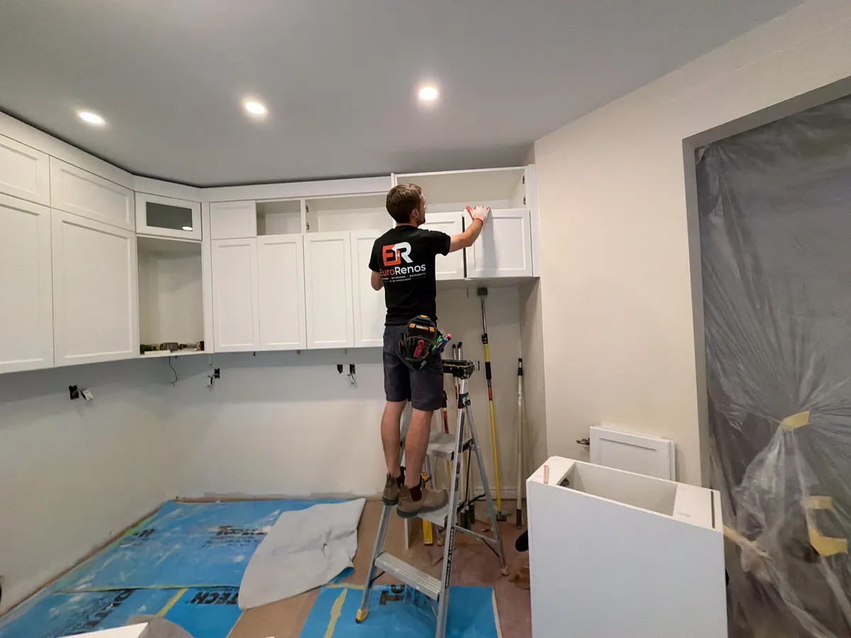An installer hanging a white shaker upper cabinet on site