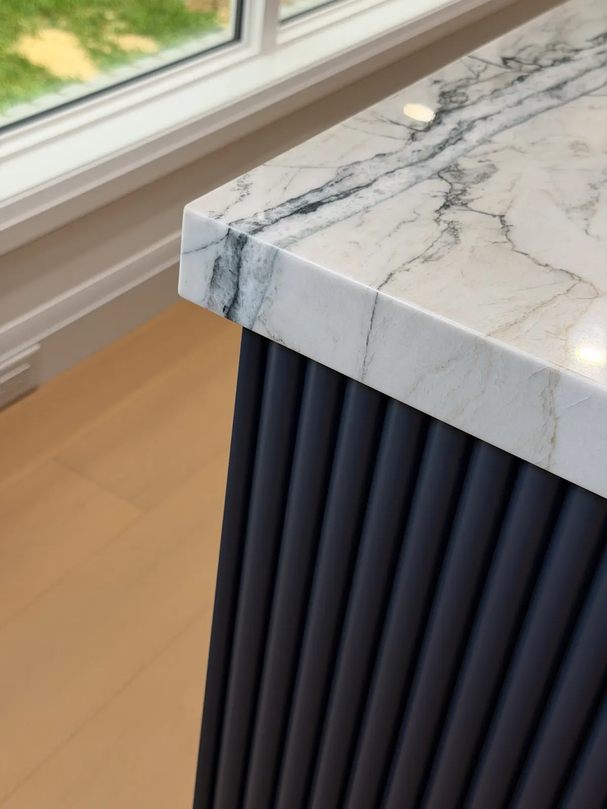Close-up of a marble waterfall edge meeting a fluted navy island panel