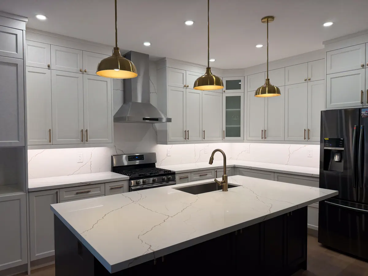 White kitchen with brass pendants over a dark quartz island