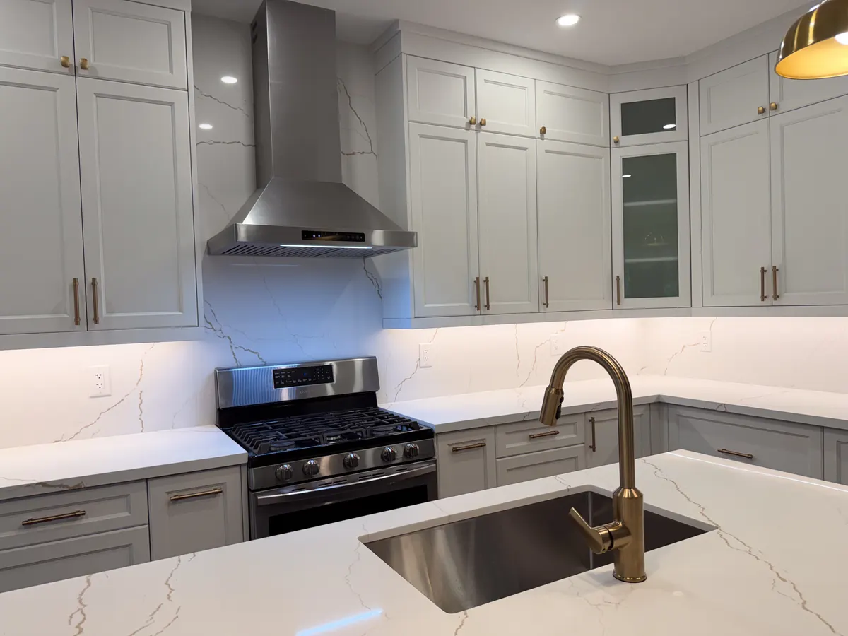 White shaker kitchen with a stainless hood and brass gooseneck tap