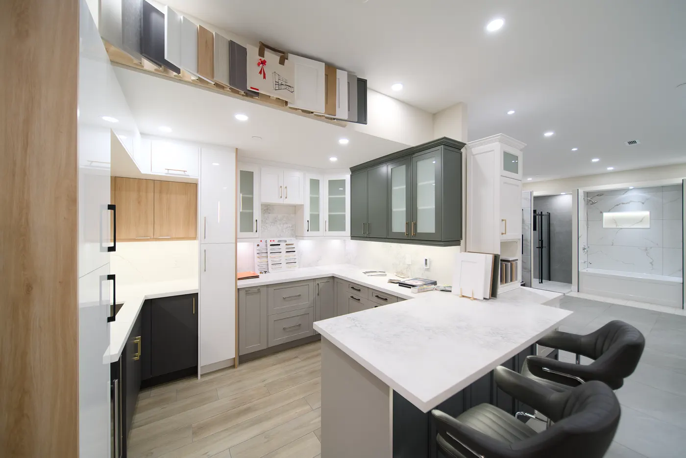 Wide view across the showroom floor: white, green and two-tone kitchen displays, door samples hung overhead, and a tiled bathroom display beyond