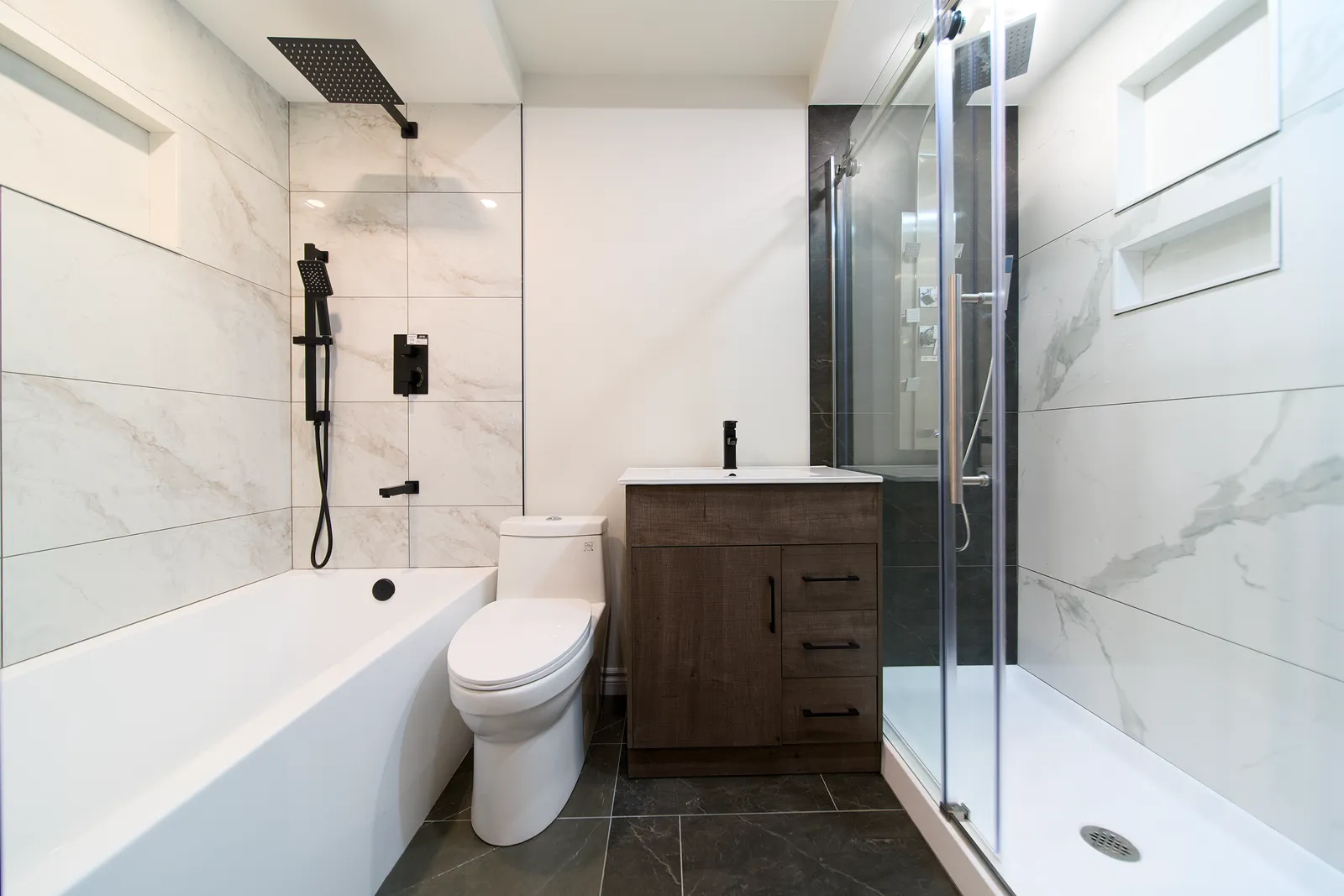 Bathroom display in the Mississauga showroom: marble-look tile with black fixtures, a freestanding tub and a glass shower