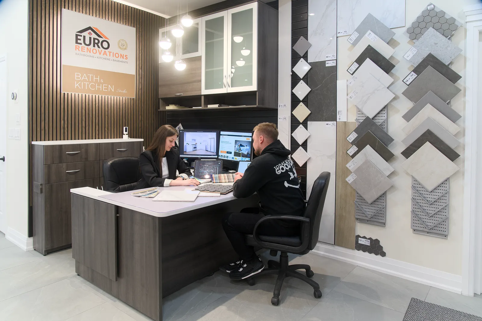 A homeowner going through a design at the showroom desk with two of our team, the tile samples on the wall behind
